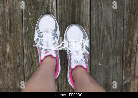 Füße mit Turnschuhen auf ihnen stehen auf einer Holzterrasse. Tennis Schuhe Stockfoto