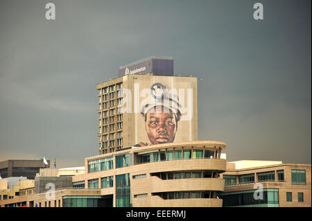 Aus der Ferne betrachtet ein Bergarbeiter-Gesicht auf einem Wolkenkratzer in Johannesburg Central Business District. Stockfoto