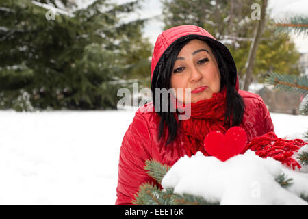 Schwarze behaarte türkische verärgert Frauen betrachten rotes Herz auf Schnee und feiern den Valentinstag alleine Stockfoto