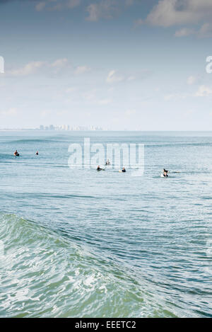 Sieben surfer Line up auf ihren Surfbrettern an einem sonnigen Tag wartet eine Welle als dünung Rollen durch mit der Daytona Beach, FL Skyline im Hintergrund zu fangen. Stockfoto