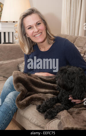 Eine Dame auf dem Sofa mit ihrem Haustier Hund, einen kleinen schwarzen Cockapoo Welpen Stockfoto