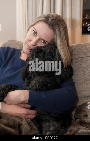Eine Dame auf dem Sofa mit ihrem Haustier Hund, einen kleinen schwarzen Cockapoo Welpen Stockfoto