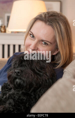 Eine Dame auf dem Sofa mit ihrem Haustier Hund, einen kleinen schwarzen Cockapoo Welpen Stockfoto