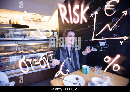 Eine junge, lächelnde Frau in einem Café mit wirtschaftlichen Symbole und Formeln zu jonglieren. Stockfoto