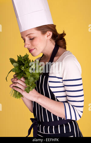Porträt eines attraktiven Köchin über einem gelben Hintergrund mit frischen Kräutern. Stockfoto