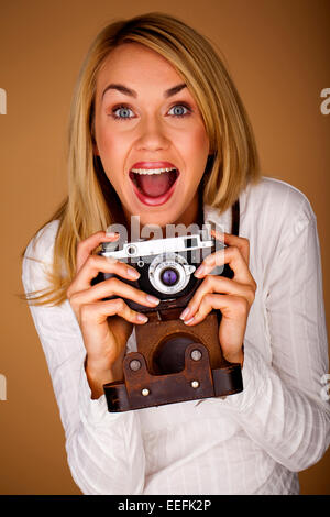 Fotografin hält eine Vintage-Kamera über einen braunen Hintergrund. Stockfoto
