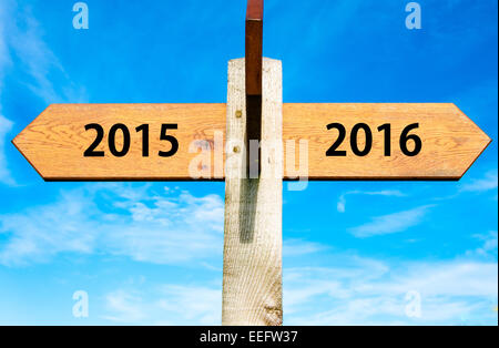 Wegweiser aus Holz mit zwei entgegengesetzte Pfeile über klaren, blauen Himmel, Jahr 2015 und 2016 Zeichen, Happy New Year Konzeptbild Stockfoto