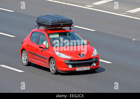 Seitlicher Frontsicht, Fahrer in rotem Vauxhall-Auto mit großem schwarzem Dachgepäckfach, der auf der Autobahn M25 Essex England UK fährt Stockfoto