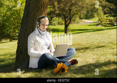 Frau Musikhören während der Arbeit am Laptop im park Stockfoto