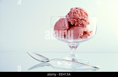 Erdbeereis Kugeln in eine schlichte Glasschale mit einem Löffel auf weißem Hintergrund in einem studio Stockfoto