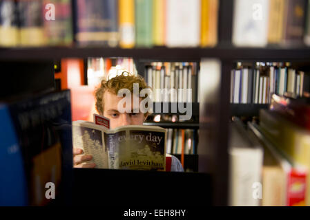 Ein junger Mann liest ein Buch von David Levithan in einer öffentlichen Bibliothek Stockfoto