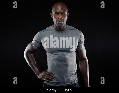 Porträt von muskulösen jungen Mann in Sportbekleidung Blick in die Kamera vor schwarzem Hintergrund. Starken afrikanischen Sportler posieren zuversichtlich