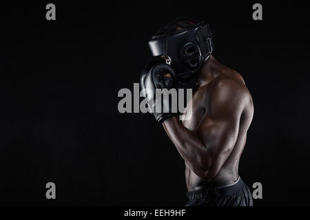 Seitenansicht eines jungen männlichen Boxer in eine Kampfposition auf schwarzem Hintergrund. Afrikanische männlichen Boxer sein Gesicht mit Handschuhen zu blockieren. Stockfoto