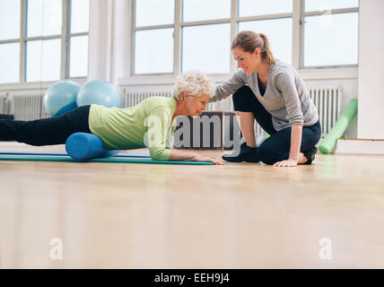 Ältere Frau mit einer Schaumrolle wird unterstützt durch personal Trainer im Fitness-Studio trainieren. Physiotherapeuten helfen senior Frau Stockfoto