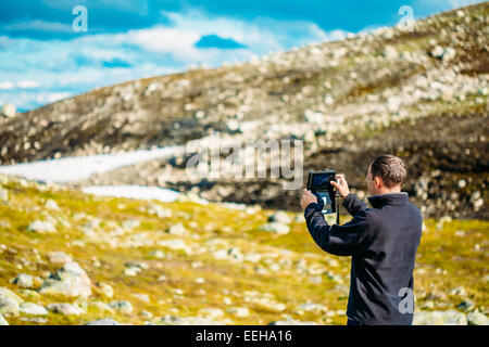 Junger Mann Fotografieren der norwegische Berglandschaft auf mobilen Gerät Tablet. Norwegens Natur Stockfoto