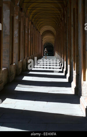 Eine Frau mit Sonnenbrille spaziert der Portico di San Luca in Bologna, Italien. Angeblich die längste Säulenhalle der Welt. Stockfoto