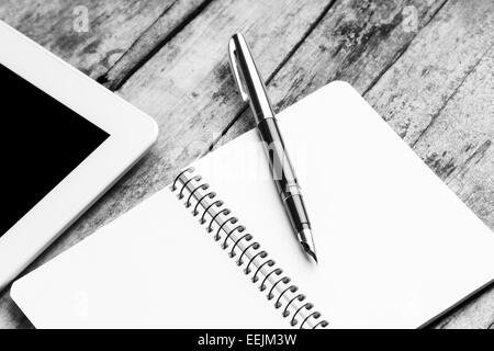 Freier Arbeitsplatz mit Tablet-PC, geöffneten Notizbuch und Retro-Füllfederhalter auf rustikalen Holztisch.  Schwarz / weiß Bild Stockfoto