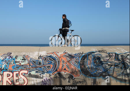 Mann mit Fahrrad entlang bedeckt Graffitiwand neben Meer, in der Nähe von Badalona, Barcelona Stockfoto