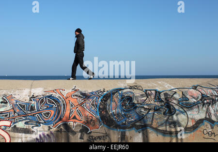 Mann zu Fuß entlang bedeckt Graffitiwand neben Meer, in der Nähe von Badalona, Barcelona Stockfoto