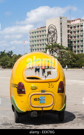 Gelbe coco Taxi an das Ministerium des Innern Gebäude geparkt mit Bild von Che Guevara an der Plaza de la Revolución, Havanna, Kuba Stockfoto