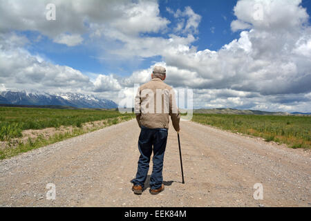 Neunzig Jahre alten Mann mit einem Stock zu Fuß entfernt von der Kamera auf einer langen geraden Straße. In Jackson Hole, Wyoming. Stockfoto