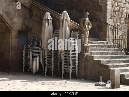 Statue und Schritte neben gestapelten Stühle und gefalteten Regenschirme in den Gärten des alten Hospital De La Santa Creu, El Raval, Barcelona Stockfoto