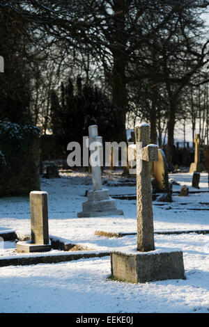 Grabstein Kreuz im Schnee auf einem Friedhof. Cotswolds, England Stockfoto