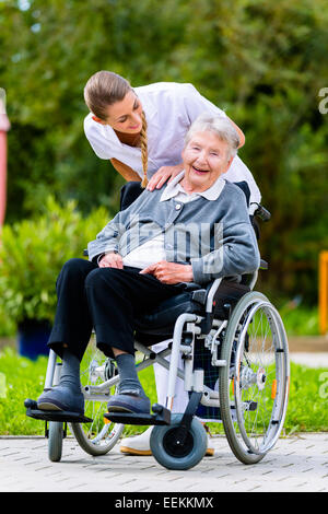 Krankenschwester drängen ältere Frau im Rollstuhl auf Spaziergang durch den Garten im Sommer Stockfoto