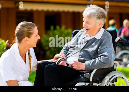 Krankenschwester drängen ältere Frau im Rollstuhl auf Spaziergang durch den Garten im Sommer Stockfoto