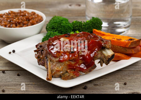 Nahaufnahme von gegrillte spare Ribs mit Süßkartoffel-Pommes-frites, Brokkoli, Bohnen und Glas Wasser am rustikalen Holztisch. Stockfoto