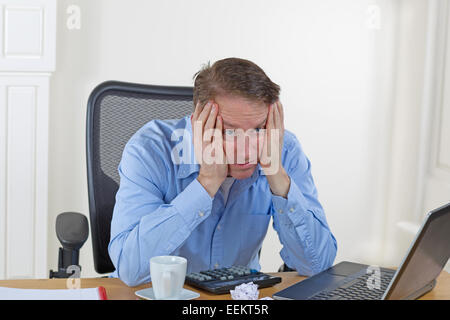 Reifer Mann mit Kopf in den Händen während der Suche mit Laptop, Rechner, gebrochene Stifte, wattierte Papier, Kaffeetasse und keine verloren Stockfoto