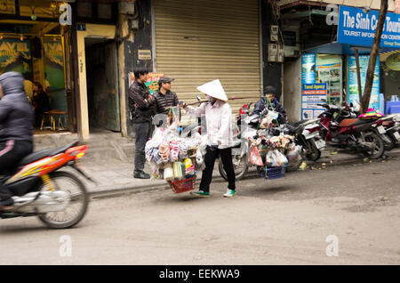 Frau Straßenhändler trägt zwei Körbe mit verschiedenen Dingen in Plastiktüten an jedem Ende der Pole, in der Straße aufgehängt Stockfoto