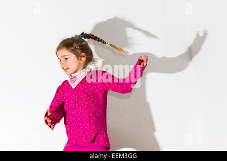Mädchen, 3 Jahre, trägt ein rosa Hemd, tanzen, wirft einen Schatten auf einer weißen Wand Stockfoto