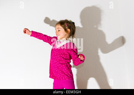 Mädchen, 3 Jahre, trägt ein rosa Hemd, tanzen, wirft einen Schatten auf einer weißen Wand Stockfoto