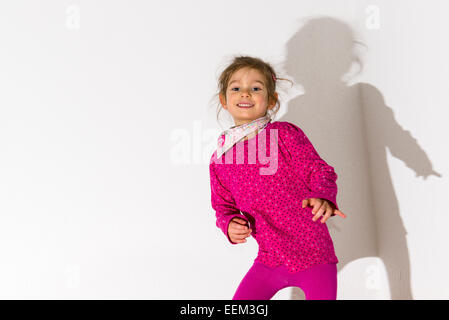 Mädchen, 3 Jahre, trägt ein rosa Hemd, tanzen, wirft einen Schatten auf einer weißen Wand Stockfoto