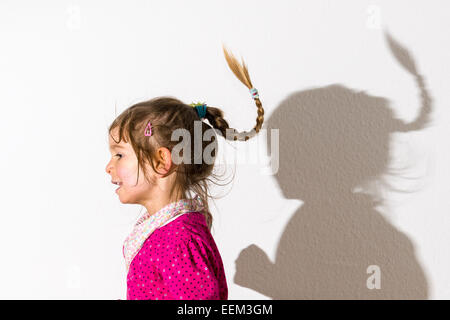 Mädchen, 3 Jahre, trägt ein rosa Hemd, tanzen, wirft einen Schatten auf einer weißen Wand Stockfoto