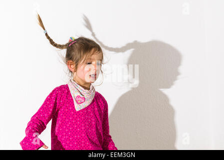 Mädchen, 3 Jahre, trägt ein rosa Hemd, tanzen, wirft einen Schatten auf einer weißen Wand Stockfoto