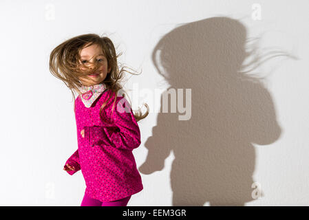 Mädchen, 3 Jahre, trägt ein rosa Hemd, tanzen, wirft einen Schatten auf einer weißen Wand Stockfoto