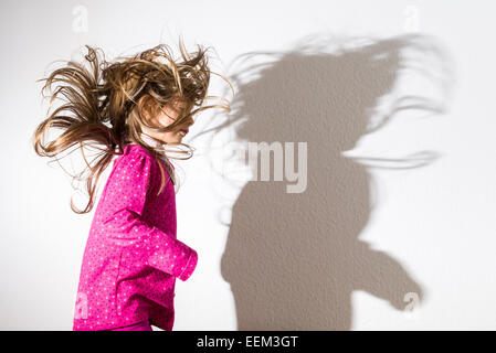 Mädchen, 3 Jahre, trägt ein rosa Hemd, tanzen, wirft einen Schatten auf einer weißen Wand Stockfoto