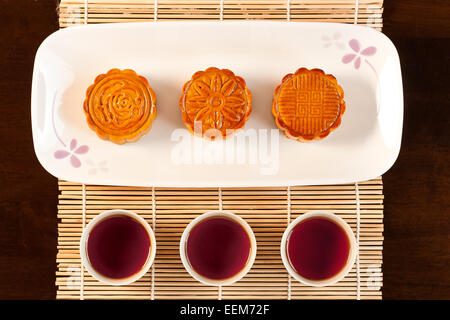 Drei Tassen Tee und drei Mooncakes auf weißem Teller serviert Stockfoto