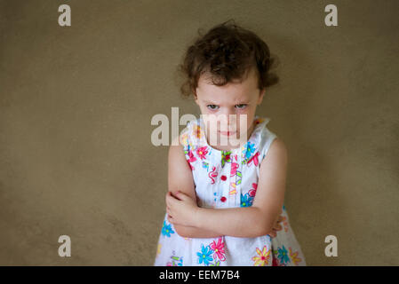 Mürrischen Mädchen (2-3) in floral gemustertes Kleid tatenlos Wand mit Arme gekreuzt Stockfoto