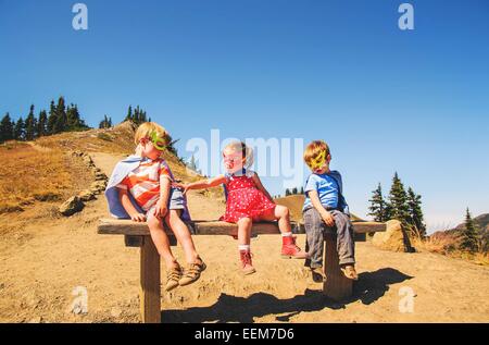 Drei Kinder, die als Superhelden verkleidet auf einer Bank sitzen Stockfoto