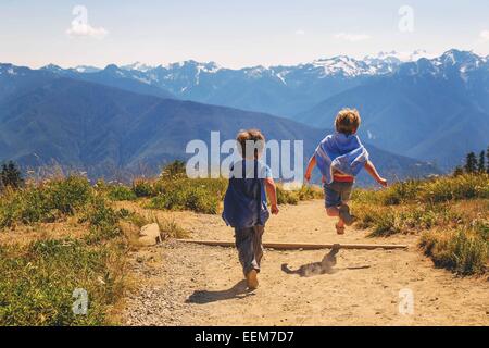 Zwei Jungen, die als Superhelden verkleidet sind, laufen auf einem Bergpfad Stockfoto