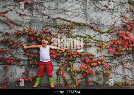 Junge, der gegen eine Efeu bedeckte Wand steht, USA Stockfoto