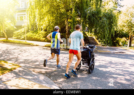 Kaukasische schwules Paar Joggen mit Kinderwagen in Nachbarschaft Stockfoto