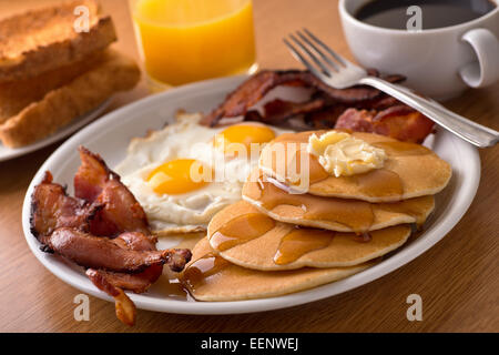 Ein leckeres Hauptart Frühstück mit knusprigem Speck, Eiern, Pfannkuchen, Toast, Kaffee und Orangensaft. Stockfoto