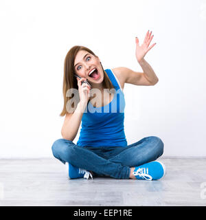 Überrascht, junge Frau auf dem Boden sitzen und telefonieren Stockfoto