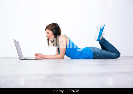 Lächelnde Frau mit Kopfhörern auf dem Boden liegend mit laptop Stockfoto