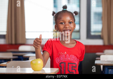 Junge Afro amerikanische schwarze Mädchen Klassenzimmer Rezeption lächelnd mit einem grünen Apfel. Stockfoto