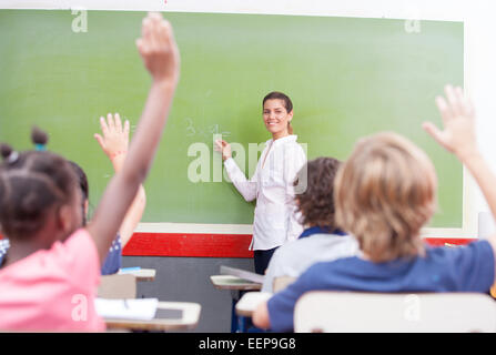 Intelligente Gruppe von jungen Schulkindern Erziehung ihrer Hände in der Luft, von der Lehrerin, Ansicht eine Frage zu beantworten Stockfoto